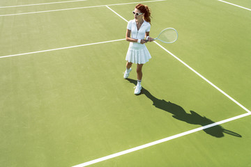 side view of young attractive woman in white tennis uniform playing tennis on court