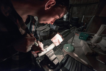 Young man carving wood in dark barn.