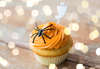 food, baking and holidays concept - cupcake or muffin with halloween party decorations on wooden...