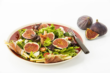 gemischter Blattsalat mit Feigen, Tomaten, Schafskaese und Crossinis mit Schinken auf roten Teller, Freisteller