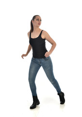 full length portrait of brunette girl wearing black single and jeans. standing pose facing the camera. isolated on white studio background.