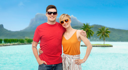 travel, tourism and summer holidays concept - smiling couple in sunglasses hugging at touristic resort over bora bora island beach background - obrazy, fototapety, plakaty
