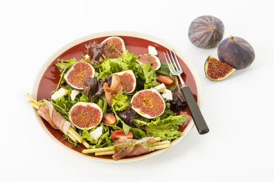 gemischter Blattsalat mit Feigen, Tomaten, Schafskaese und Crossinis mit Schinken auf roten Teller, Freisteller