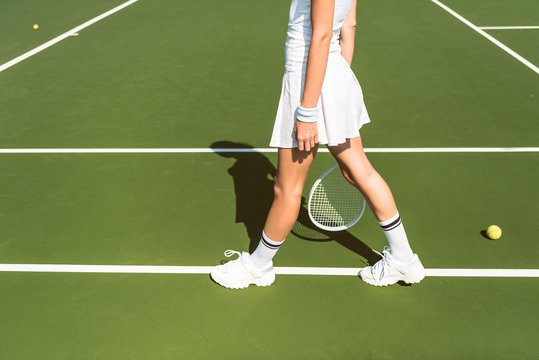 partial view of female tennis player in white sportswear with racket on tennis court
