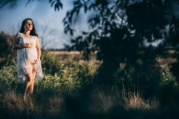 pregnant girl at sunset in loose dress in nature