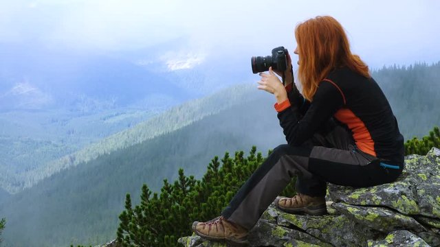 Young woman hiker taking a photo on the top of forested mountains