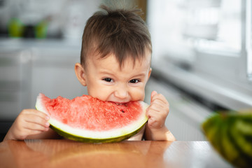 Cute little boy eating watermelon in the kitchen, very cute