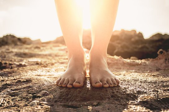 The bright sun shines between the naked feet of a woman standing on the rocks