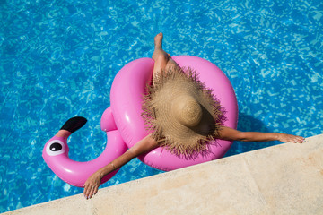 Mujer en la piscina sentada sobre un flamingo rosa con sombrero. Vista superior