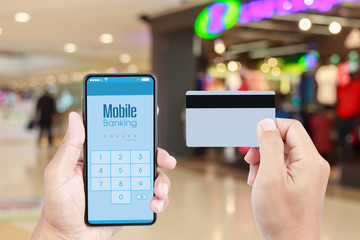 Hand holding smartphone with Mobile Banking on screen over blurred in shopping mall background for online payment via credit card
