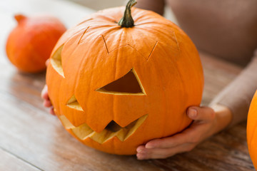 halloween, decoration and holidays concept - close up of woman with carved pumpkin or jack-o-lantern at home