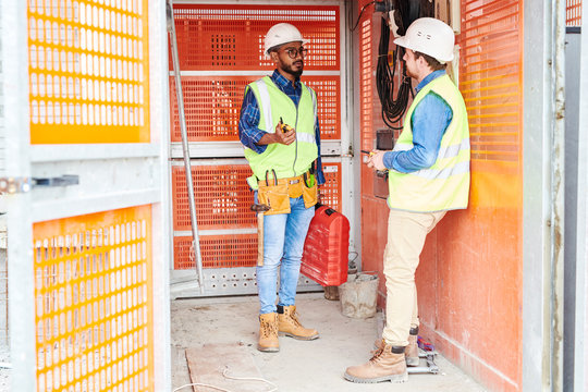 Full length portrait of two construction workers communicating while standing in elevator on site, copy space