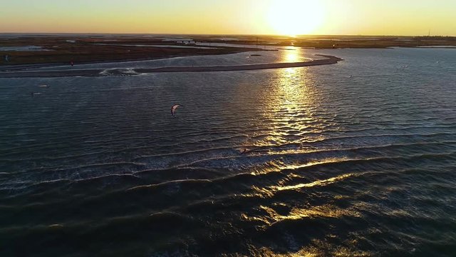 View from the height of how the kitesurfers glide on the waves at sea during the dawn, slow motion
