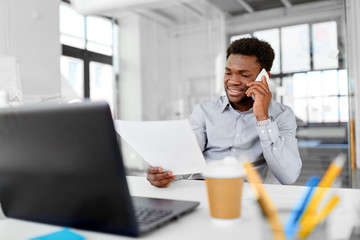 business, people, communication and technology concept - smiling african american businessman with papers and laptop computer calling on smartphone at office