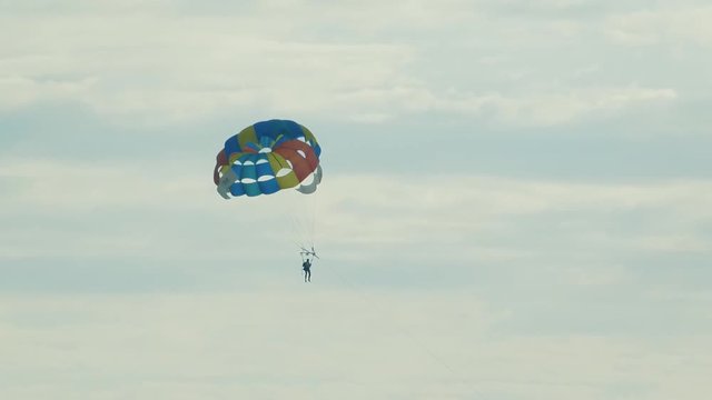 Parasailing high in the blue sky. Tourist silhouette fly under multicolored parachute. Black sea coast. Cloudy summer day.