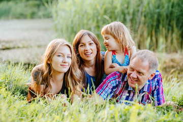 Ideal picture of family happiness - happy family with two daughter having fun and lying on the grass in lake shore on a summer day in sunset. Parenthood, love, vacation and happy family concept.