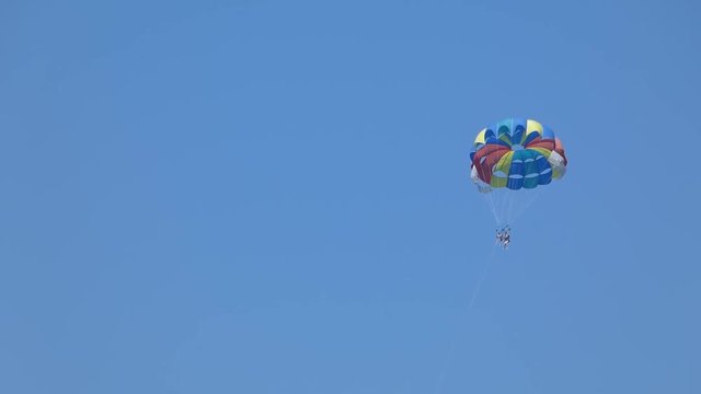 Parasailing high in the blue sky. Two tourists fly under bright multicolored parachute. Black sea coast. Sunny summer day.