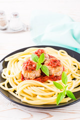 Spaghetti and meatballs in tomato sauce with fresh basil leaves on a plate