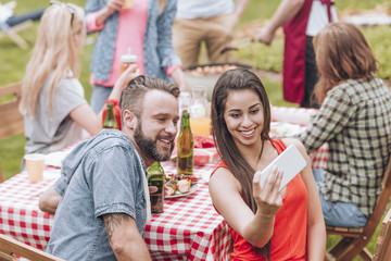 Fototapeta premium A young couple taking a selfie photo at a weekend BBQ party outside.