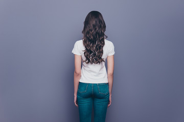 Rear back behind view of attractive pretty adorable stylish curly-haired girl in jeans and t-shirt,...