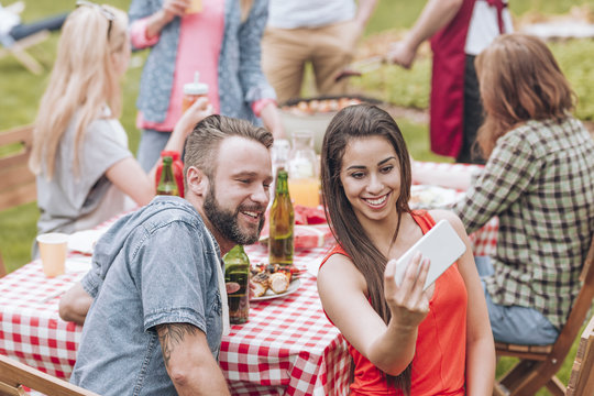 A young couple taking a selfie photo at a weekend BBQ party outside.
