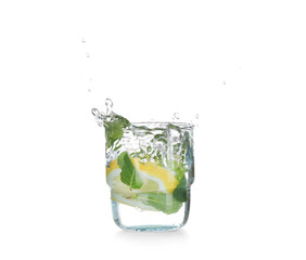 Glass with splashing water and sliced citrus fruit on white background