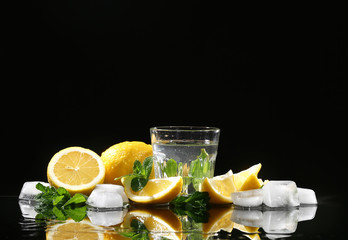 Glass of water with mint leaves, sliced lemon and ice cubes on black background
