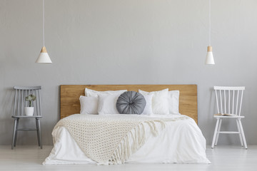 Blanket on wooden bed between chairs in grey bedroom interior with lamps and plant. Real photo - obrazy, fototapety, plakaty