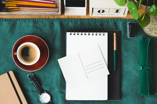 Top view of a coffee, notepad, postcard and watch on the green cloth