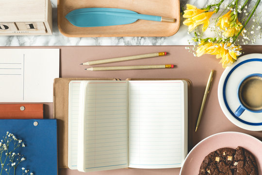 Notebook, pencils, flowers and pen in the shape of feather on a creative desk. Top view
