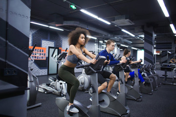 Young people doing exercises on elliptical trainer in gym - obrazy, fototapety, plakaty