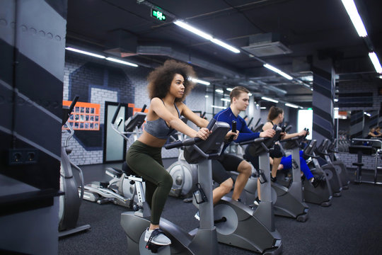 Young people doing exercises on elliptical trainer in gym