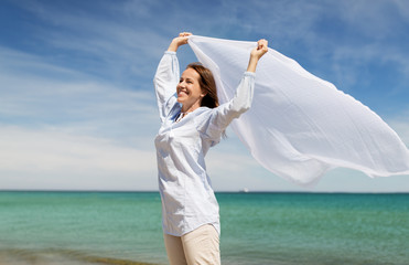 Fototapeta na wymiar people and leisure concept - happy woman with shawl waving in wind on summer beach