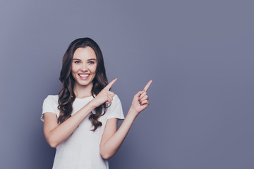 Portrait of magnificent nice lovely gorgeous adorable stylish cheerful glad curly-haired girl in casual white t-shirt, pointing aside up with two hands, copy-space, isolated over grey background