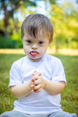 Portrait of Cute small boy with Down syndrome playing in summer day on nature