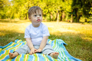 Portrait of Cute small boy with Down syndrome playing on blanket in summer day on nature