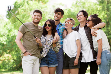 friendship, leisure and technology concept - group of happy smiling friends taking picture by selfie stick at summer park