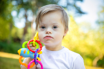 Portrait of Cute small boy with Down syndrome playing in summer day on nature with toys