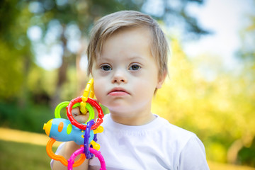 Portrait of Cute small boy with Down syndrome playing in summer day on nature with toys