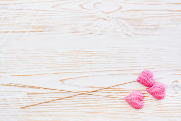 Three pink knitted hearts on sticks on a white wooden background. Copy space