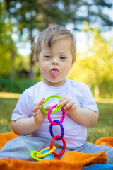 Portrait of Cute small boy with Down syndrome playing on blanket in summer day on nature with toys
