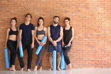 Fototapeta na wymiar Group of people with yoga mats near brick wall