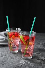Glasses with strawberry mojito on table against dark background