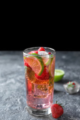 Glass with strawberry mojito on table against dark background
