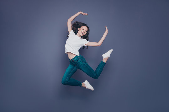 Crazy adorable pretty lovely stylish nice cheerful dreamy curly-haired brunette girl in casual white t-shirt and jeans, fooling, flying in air, isolated on grey background