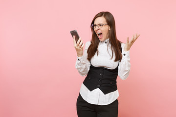 Fototapeta premium Young angry business woman in shirt, black suit, glasses screaming holding mobile phone spreading hands isolated on pink background. Lady boss. Achievement career wealth. Copy space for advertisement.