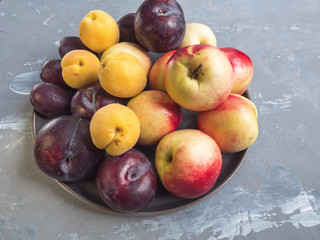ripe nectarines and red plums on a ceramic plate, top view.