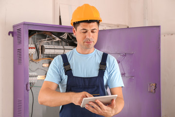 Electrician with tablet PC near distribution board indoors