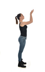  full length portrait of brunette girl wearing black single and jeans. standing pose in side profile. isolated on white studio background.