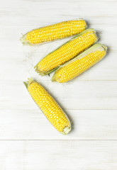 Fresh corn on cobs on white wooden table, closeup, top view, light meal background. Selective focus.